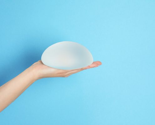 Woman holding silicone implant for breast augmentation on color