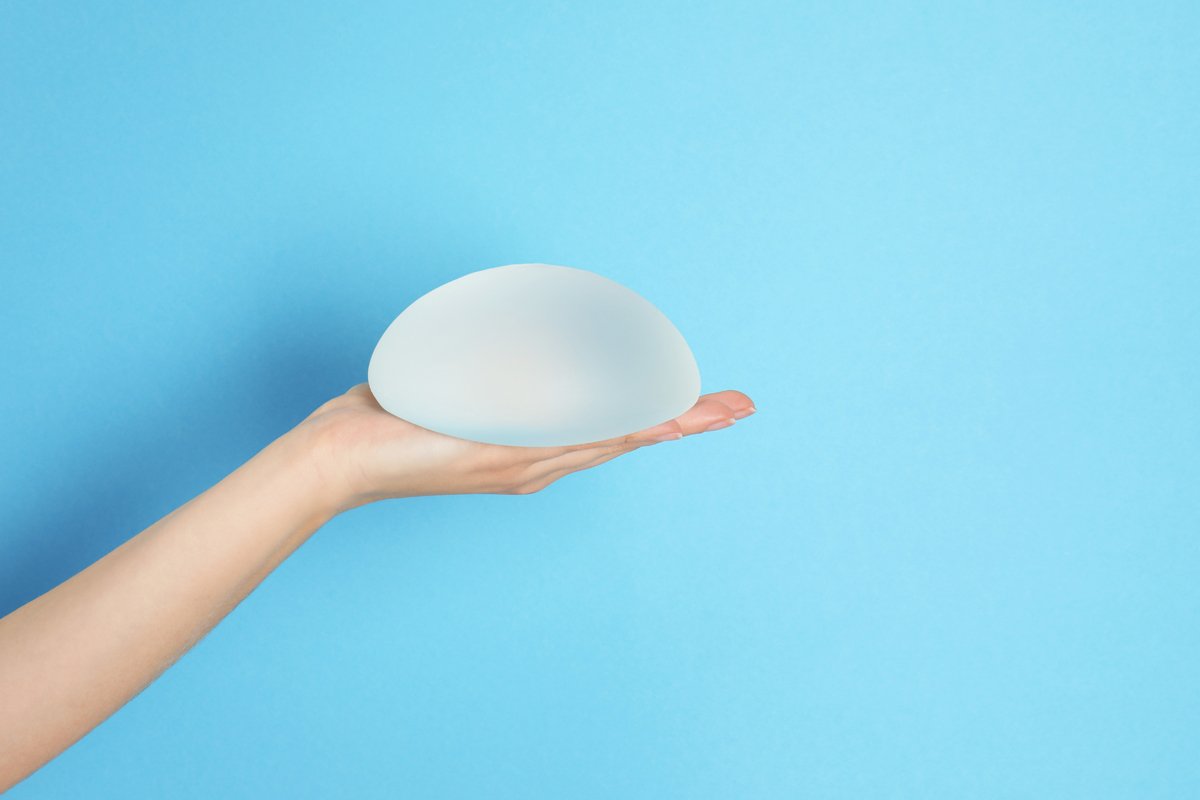 Woman holding silicone implant for breast augmentation on color