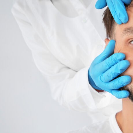 Doctor examining mature man face before cosmetic surgery on white background, closeup